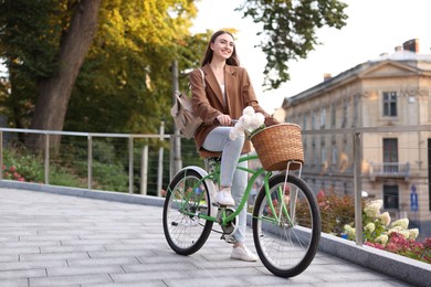 Photo of Woman riding bicycle with flowers in basket on city street. Space for text