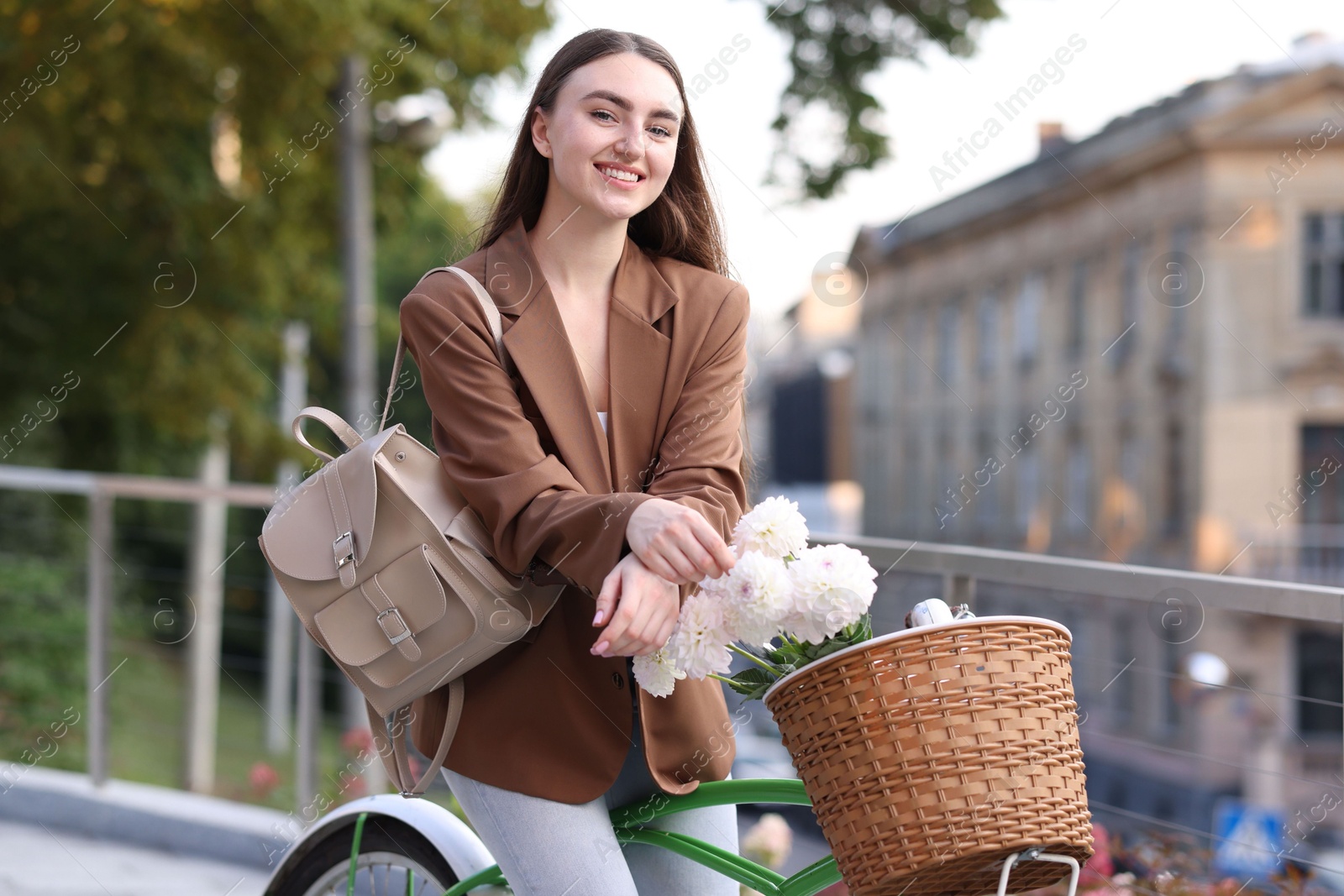 Photo of Woman riding bicycle with flowers in basket on city street