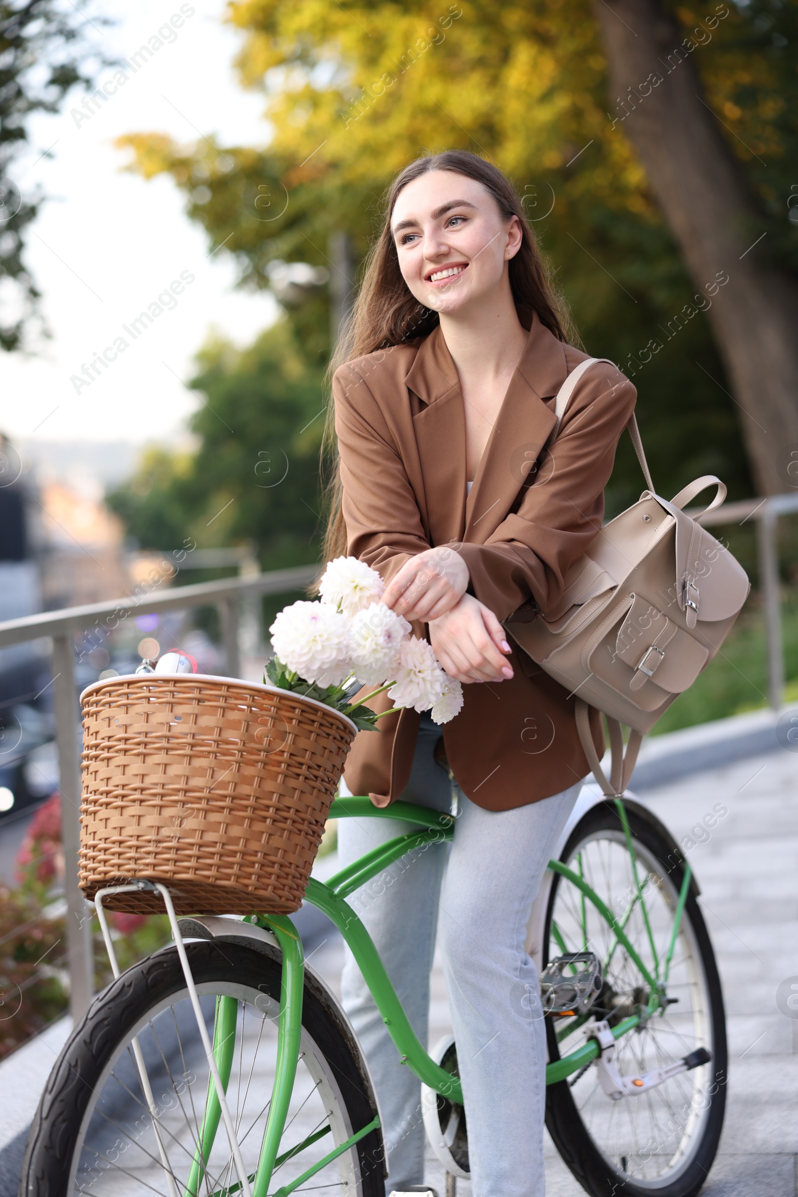 Photo of Woman riding bicycle with flowers in basket on city street