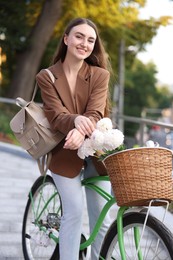 Photo of Woman riding bicycle with flowers in basket on city street