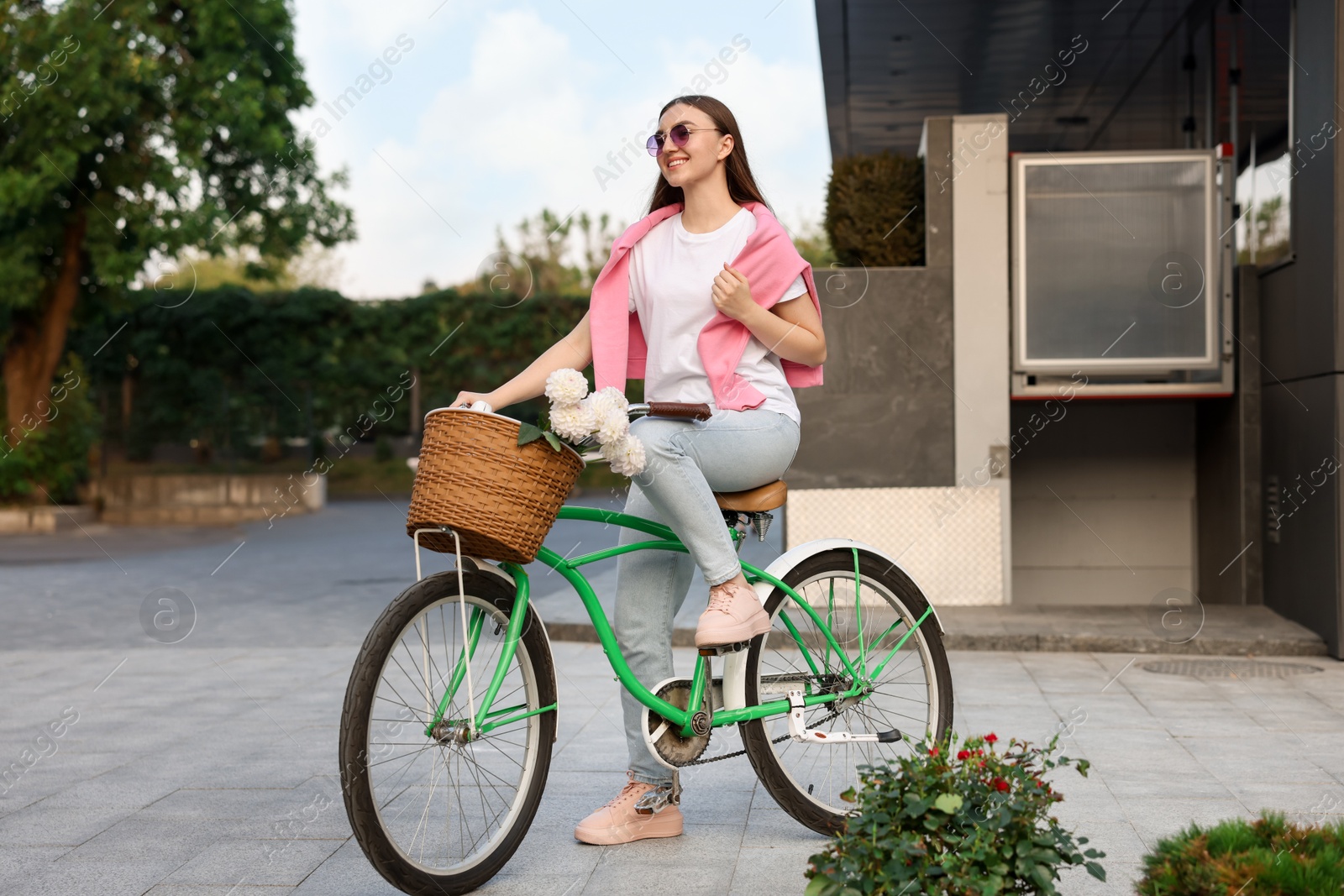 Photo of Woman riding bicycle with flowers in basket on city street