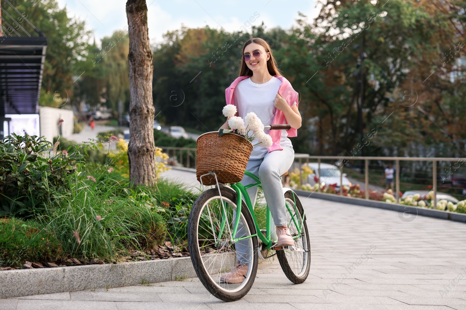 Photo of Woman riding bicycle with flowers in basket on city street