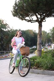 Photo of Woman riding bicycle with flowers in basket on city street