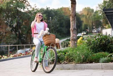 Photo of Woman riding bicycle with flowers in basket on city street. Space for text