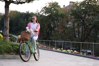 Photo of Woman riding bicycle with flowers in basket on city street. Space for text