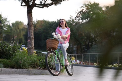 Photo of Woman riding bicycle with flowers in basket on city street