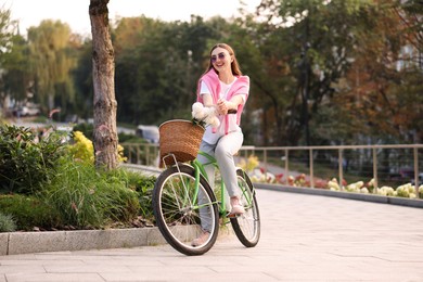 Photo of Woman riding bicycle with flowers in basket on city street