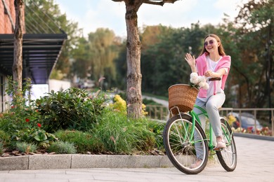 Photo of Woman riding bicycle with flowers in basket on city street. Space for text