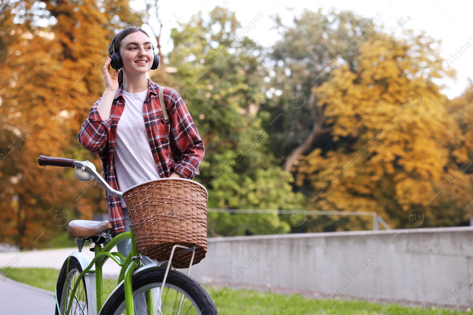 Photo of Beautiful woman listening to music while riding bicycle in park. Space for text