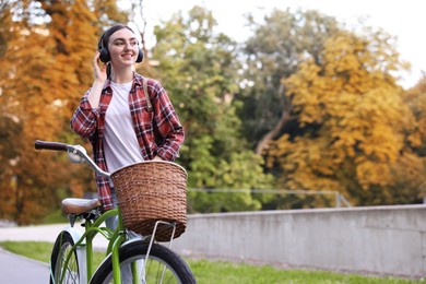 Photo of Beautiful woman listening to music while riding bicycle in park. Space for text