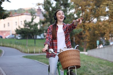 Photo of Emotional woman with headphones riding bicycle and pointing at something in park