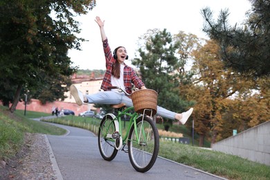 Photo of Emotional woman with headphones riding bicycle in park