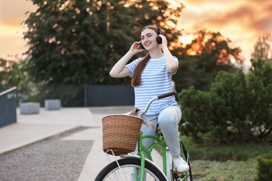 Photo of Beautiful woman listening to music while riding bicycle in park. Space for text