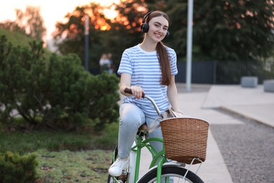 Photo of Beautiful woman listening to music while riding bicycle in park. Space for text