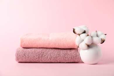 Photo of Stack of fresh terry towels and cotton flowers on pink background