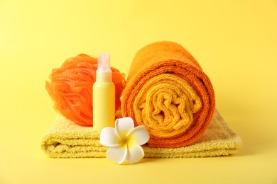 Photo of Fresh terry towels, cosmetic product, sponge and plumeria flower on yellow background