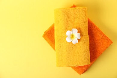 Photo of Stack of fresh terry towels and plumeria flower on yellow background, top view. Space for text