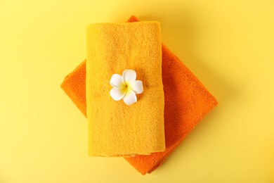 Photo of Stack of fresh terry towels and plumeria flower on yellow background, top view