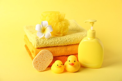 Photo of Stack of fresh terry towels, cosmetic product, rubber ducks and sponges on yellow background
