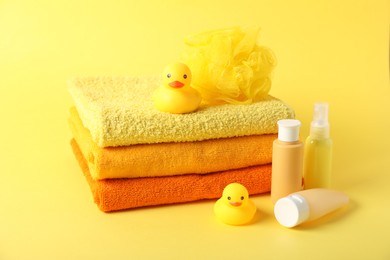 Photo of Stack of fresh terry towels, cosmetic products, rubber ducks and sponge on yellow background