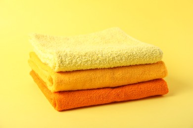 Photo of Stack of fresh terry towels on yellow background, closeup