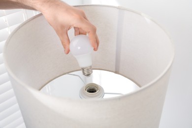 Photo of Man changing light bulb in lamp at home, closeup