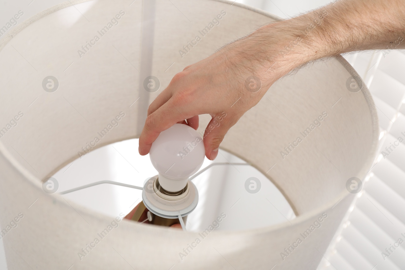 Photo of Man changing light bulb in lamp at home, closeup