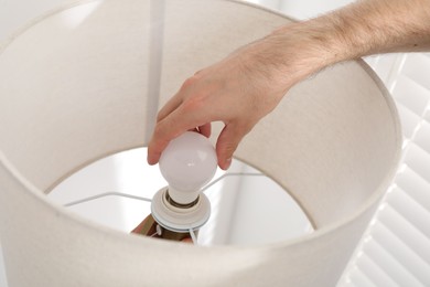 Photo of Man changing light bulb in lamp at home, closeup