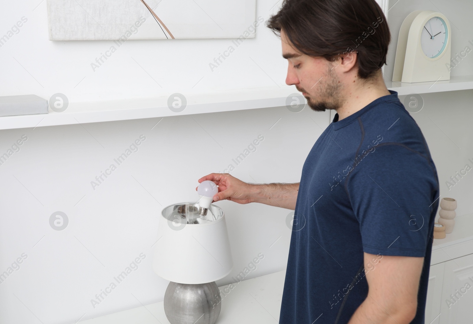 Photo of Man changing light bulb in stylish lamp indoors