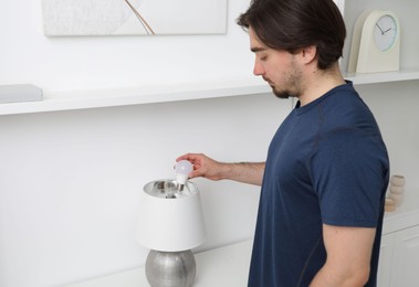 Photo of Man changing light bulb in stylish lamp indoors