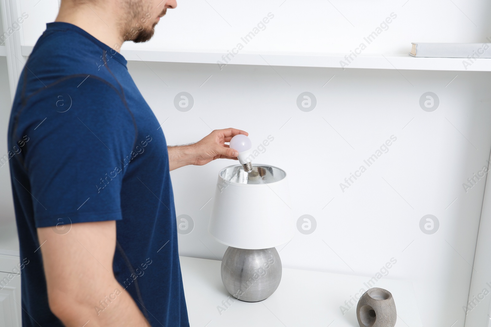 Photo of Man changing light bulb in stylish lamp indoors, closeup. Space for text