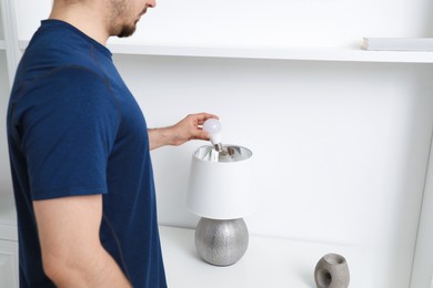 Photo of Man changing light bulb in stylish lamp indoors, closeup. Space for text