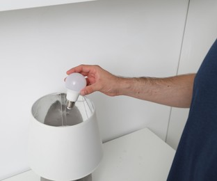 Photo of Man changing light bulb in lamp on white table, closeup
