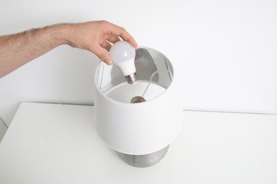 Photo of Man changing light bulb in lamp on white table, closeup