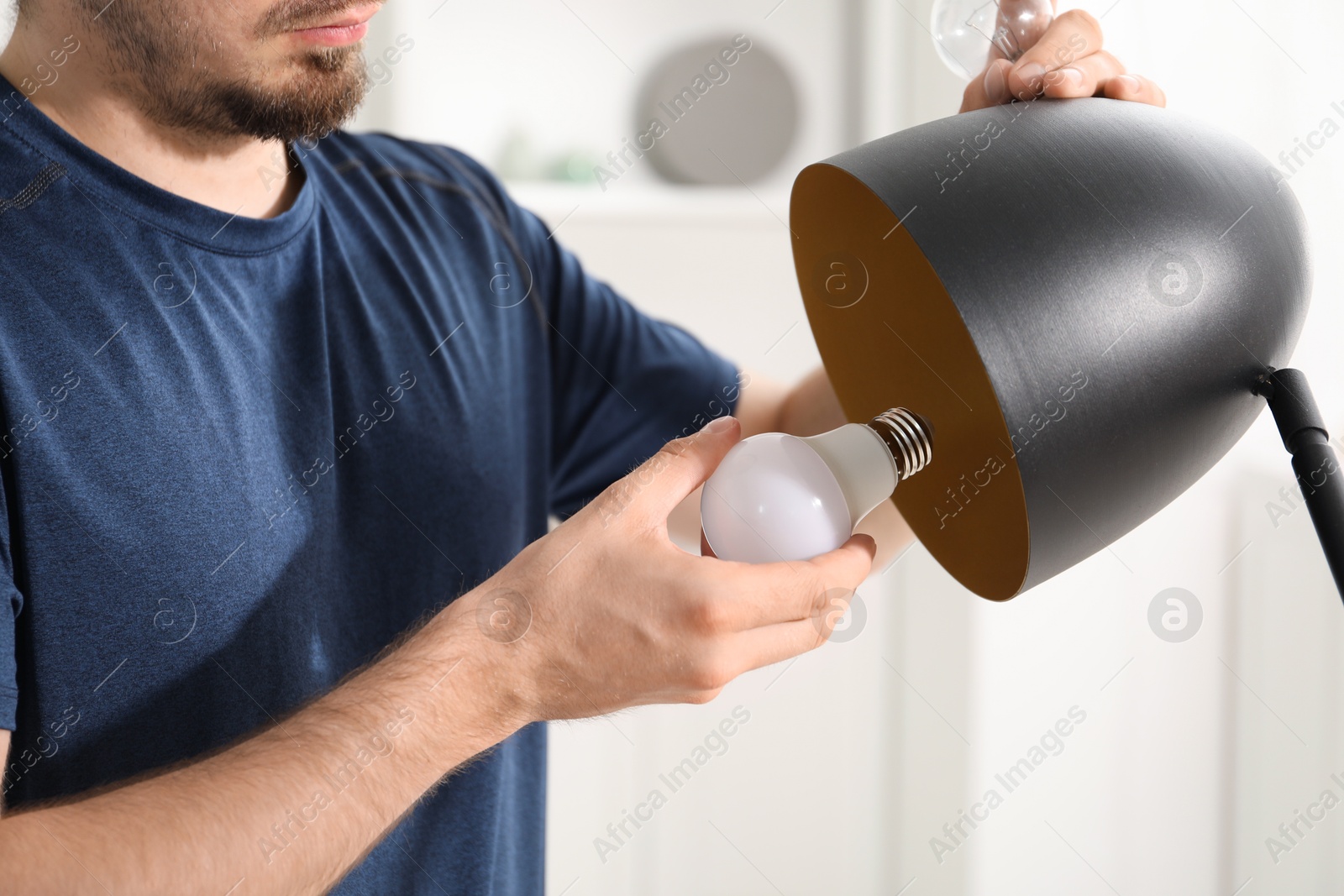 Photo of Man changing incandescent light bulb for fluorescent one in lamp at home, closeup