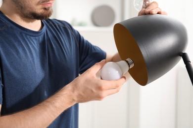 Photo of Man changing incandescent light bulb for fluorescent one in lamp at home, closeup