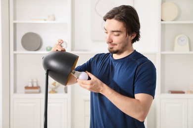 Photo of Man changing incandescent light bulb for fluorescent one in lamp at home