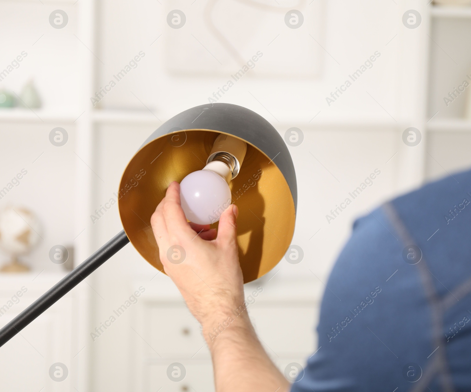 Photo of Man changing light bulb in stylish lamp at home, closeup