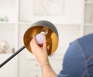 Photo of Man changing light bulb in stylish lamp at home, closeup