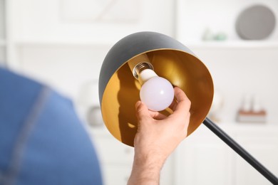 Photo of Man changing light bulb in stylish lamp at home, closeup