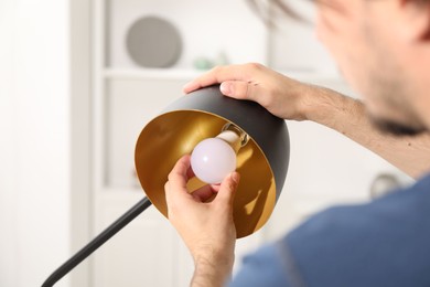 Photo of Man changing light bulb in stylish lamp at home, closeup