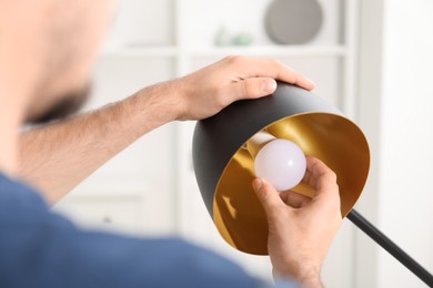 Photo of Man changing light bulb in stylish lamp at home, closeup