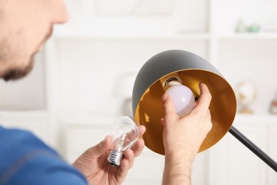 Photo of Man changing incandescent light bulb for fluorescent one in lamp at home, closeup