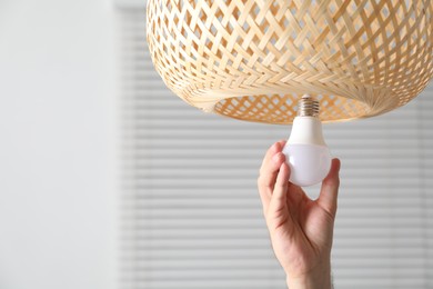 Photo of Man changing light bulb in lamp at home, closeup. Space for text
