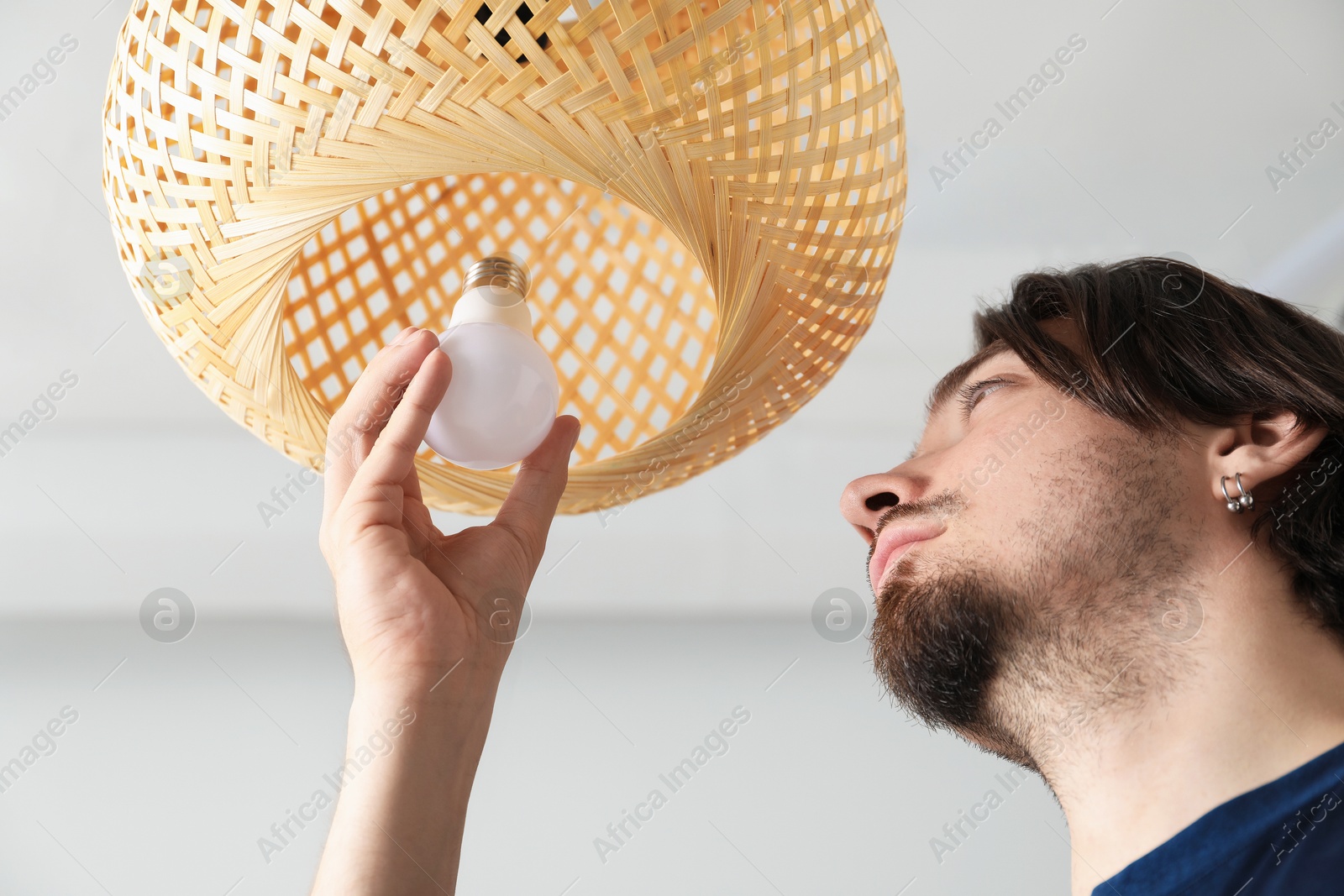 Photo of Man changing light bulb in lamp at home, low angle view