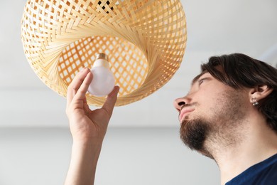 Photo of Man changing light bulb in lamp at home, low angle view