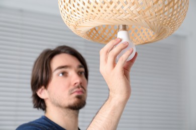 Photo of Man changing light bulb in lamp at home, selective focus