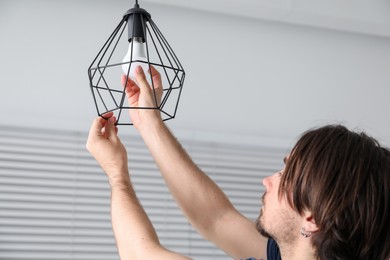 Photo of Man changing light bulb in stylish lamp indoors