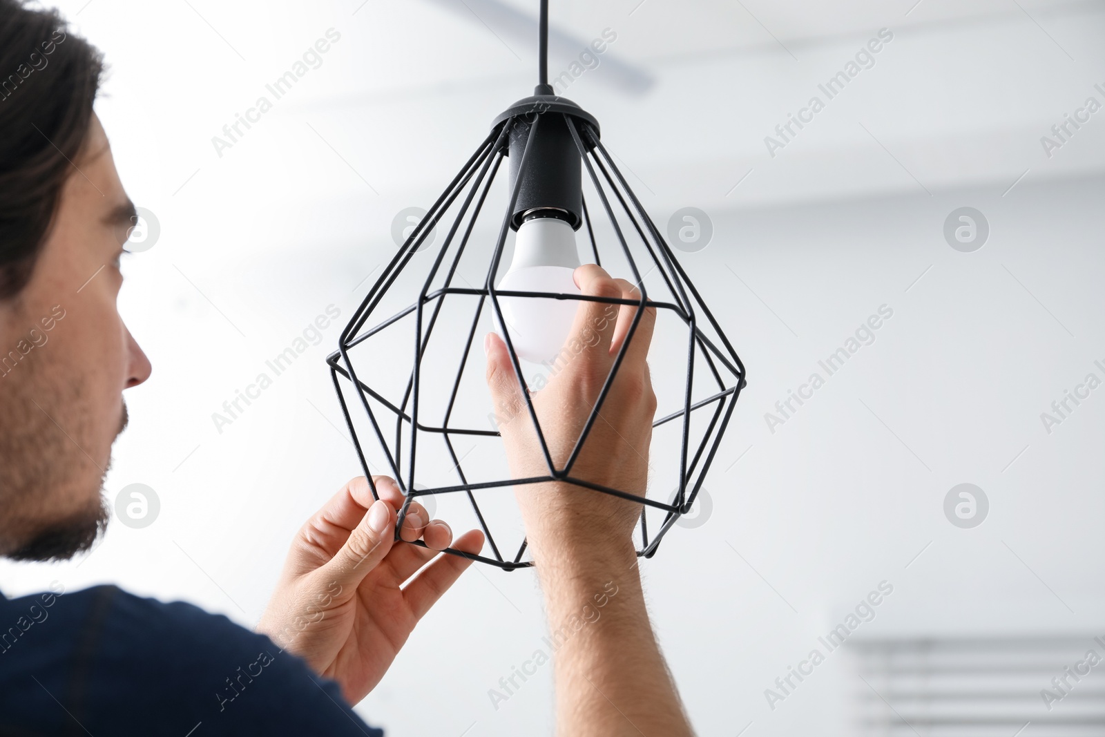 Photo of Man changing light bulb in stylish lamp indoors