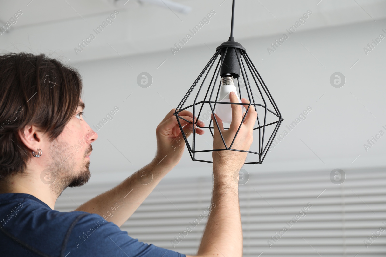Photo of Man changing light bulb in stylish lamp indoors
